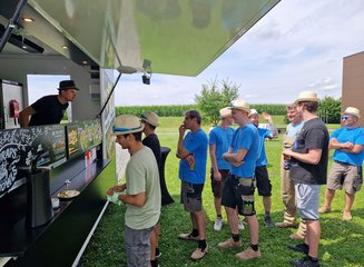 Mitarbeiter:innen der Tischlerei beim Anstellen beim Food Truck Sommerfest 2025