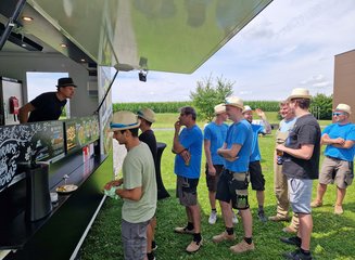Mitarbeiter:innen der Tischlerei beim Anstellen beim Food Truck Sommerfest 2025