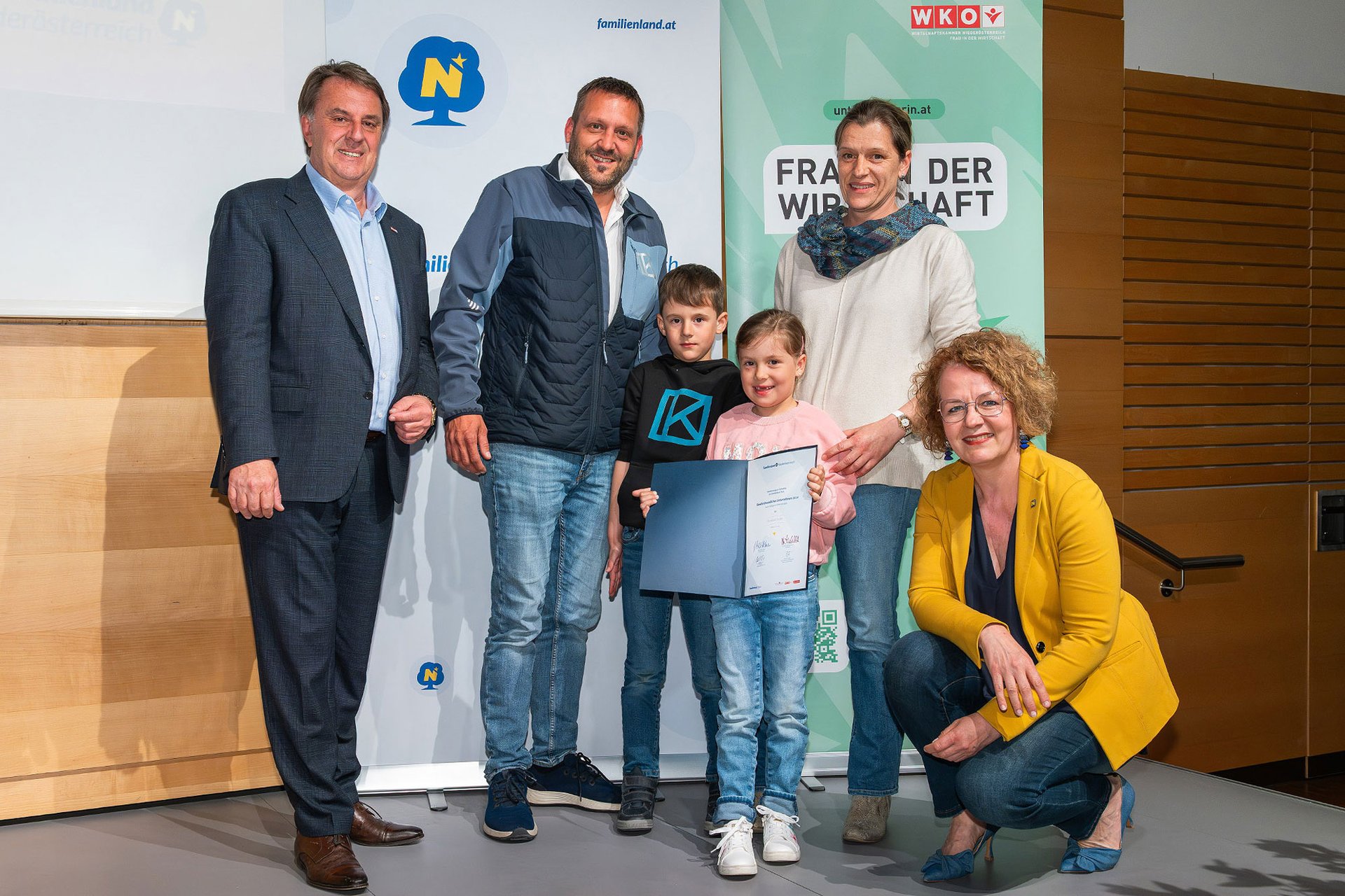 vier erwachsene Personen und zwei Kinder bei einer Preisverleihung auf einer Bühne, ein Kind hält die Urkunde in der Hand