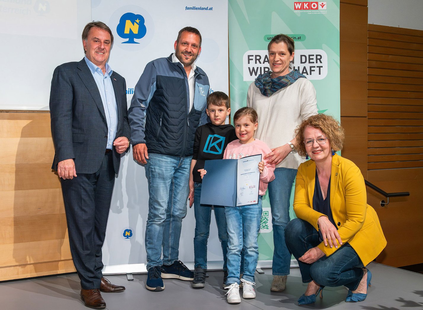 vier erwachsene Personen und zwei Kinder bei einer Preisverleihung auf einer Bühne, ein Kind hält die Urkunde in der Hand