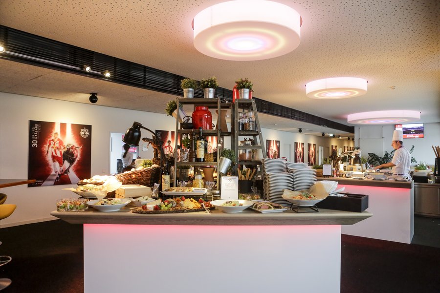 © GEPA pictures/ Jasmin Walter Buffetbereich mit zentralem, mehrstufigem Regal, dekoriert mit Pflanzen und Accessoires, umgeben von weißen Buffetpulten mit roter Unterbeleuchtung.