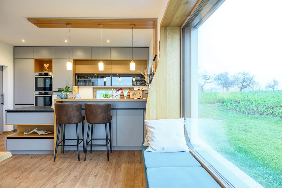 © Wolfgang Stecher/grapple.at Sitzbank vor einem großen Fenster, im Hintergrund die großzügige Wohnküche