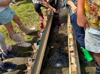 Wasserräder aus Holz werden von Kindern in einem kleinen Bach getestet Ferienabenteuer in der Tischlerei
