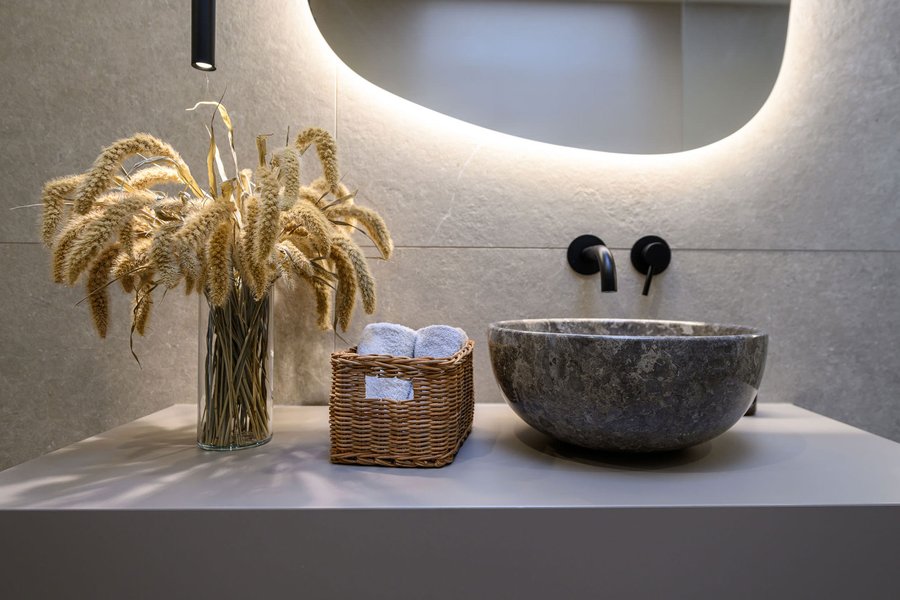 Badezimmer mit runden und hohem Waschbecken in grau, schwarze Amaturen und natürlicher Deko