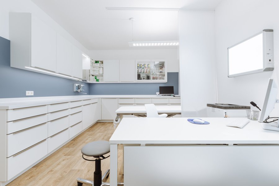 Behandlungsraum in einer Ordination mit Schreibtisch und einer großen Wand mit zahlreichen Regalen.