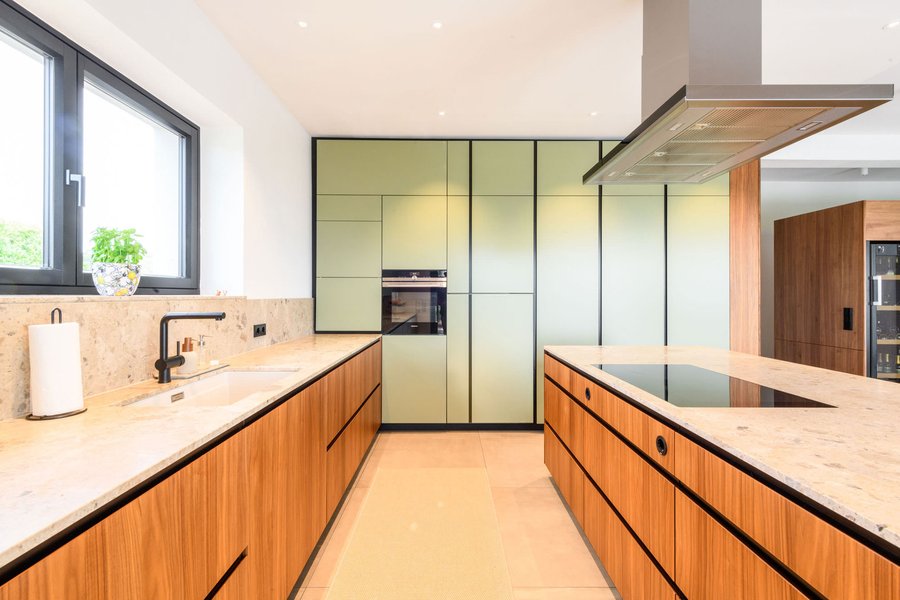 © Wolfgang Stecher/grapple.at Einbauküche mit großen Einbauschränken in grün und Holz und Arbeitsflächen in hellem Marmor