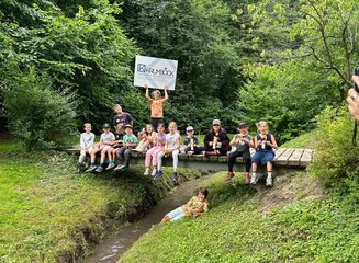 Alle Kinder der Ferienbetreuung auf einer Brücke über einem Bache bei einem Gruppenfoto. Ferienabenteuer in der Tischlerei