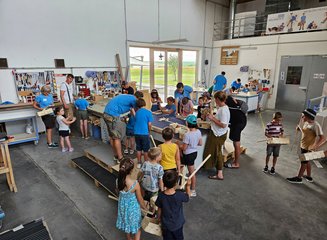 Zahlreiche Kinder und Tischler beim Arbeiten in der Werkstatt einer Tischlerei Ferienspass in deiner Traditionstischlerei