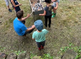 Kinder grillen gemeinsam mit einem Erwachsenen Würstel an einem Holzkohlegrill Ferienabenteuer in der Tischlerei