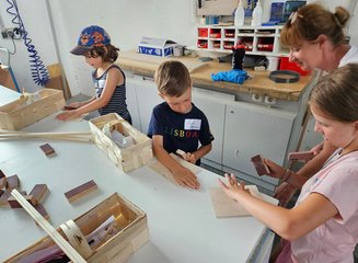 Drei Kinder arbeiten an einer Werkbank in einer Tischlerei an einem Stück Holz Ferienspass in deiner Traditionstischlerei