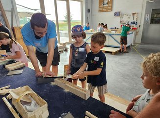 Zwei Kinder sägen gemeinsam mit einem Tischler an Holz Ferienspass in deiner Traditionstischlerei