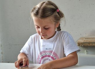 Kind in der Werkstatt einer Tischlerei beim Bearbeiten von Holz Ferienspass in deiner Traditionstischlerei