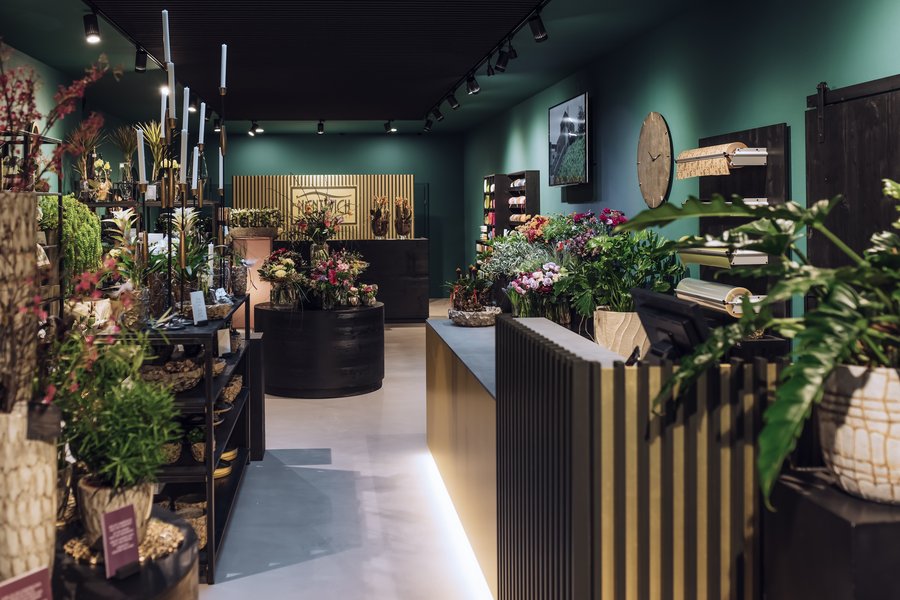 Blumengeschäft mit grauem Boden und schwarzen Regalen mit Holzelementen