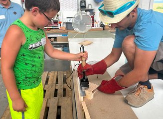 Kind mit Tischler beim Bearbeiten von Holz Ferienspass 2026: Kleine Werkstücke, große Begeisterung
