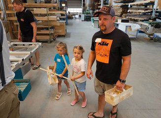 Mann und zwei Kinder gehen mit Holz durch die Werkstatt einer Tischlerei Ferienspass in deiner Traditionstischlerei
