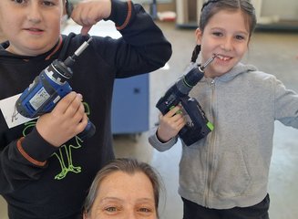 eine erwachsene Person und zwei Kinder mit Bohrmaschinen in einer Werkstatt Handwerklicher Besuch der Volksschule Hafnerbach