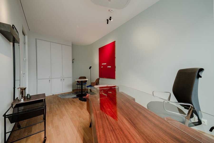 © Bureau EA Büro mit großem Schreibtisch mit Glasplatte und einem kleinen Tisch mit zwei Sesseln für Besprechungen.