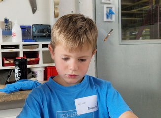 Kind in der Werkstatt einer Tischlerei beim Bearbeiten von Holz Ferienspass in deiner Traditionstischlerei