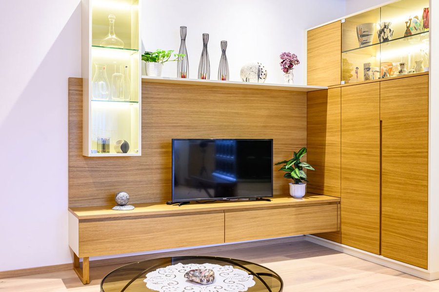© Wolfgang Stecher/grapple.at Wohnzimmerwandverbau aus Holz mit TV-Kasten, Glasvitrine und hohe Regale für Stauraum