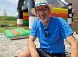 Mitarbeiter der Tischlerei mit Sommerhut sitzt vor der Hüpfburg Sommerfest 2025