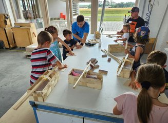 Mehrere Kinder arbeiten an einer Werkbank in einer Tischlerei an Holz Ferienspass in deiner Traditionstischlerei
