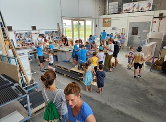 Zahlreiche Kinder und Tischler beim gemeinsamen Arbeiten in der Werkstatt in einer Tischlerei Ferienspass in deiner Traditionstischlerei
