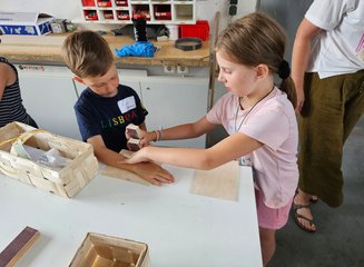 Ein weibliches und ein männliches Kind arbeiten gemeinsam an einem Stück Holz Ferienspass in deiner Traditionstischlerei