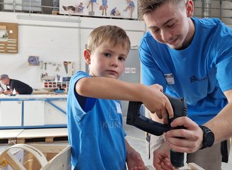 Kind in der Werkstatt einer Tischlerei beim bearbeiten von Holz Ferienspass in deiner Traditionstischlerei